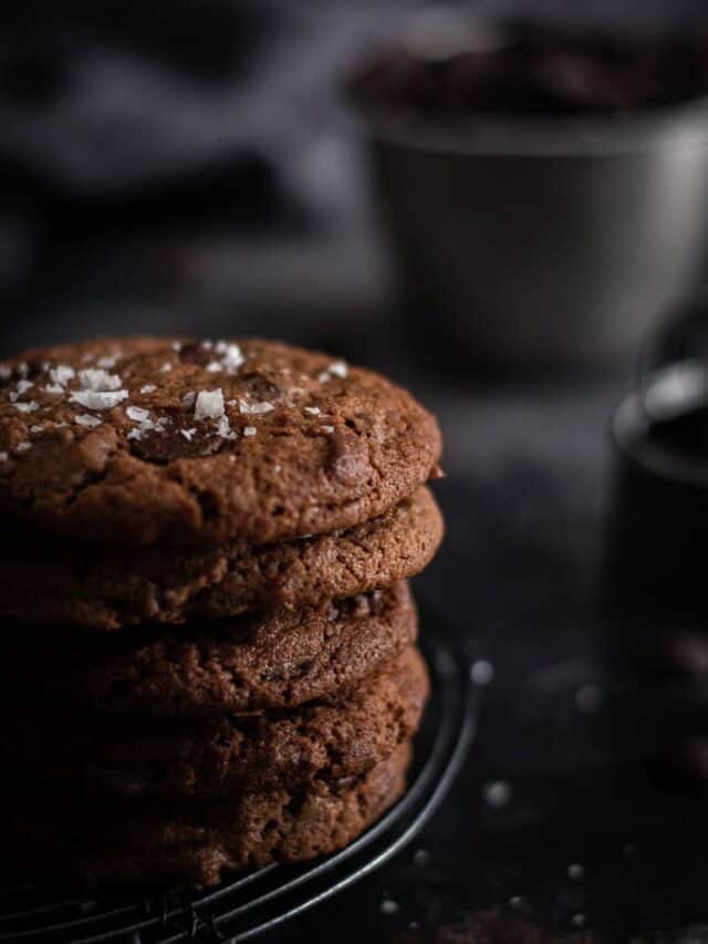 a stack of double cholate chip cookies on a black wire cooling rack