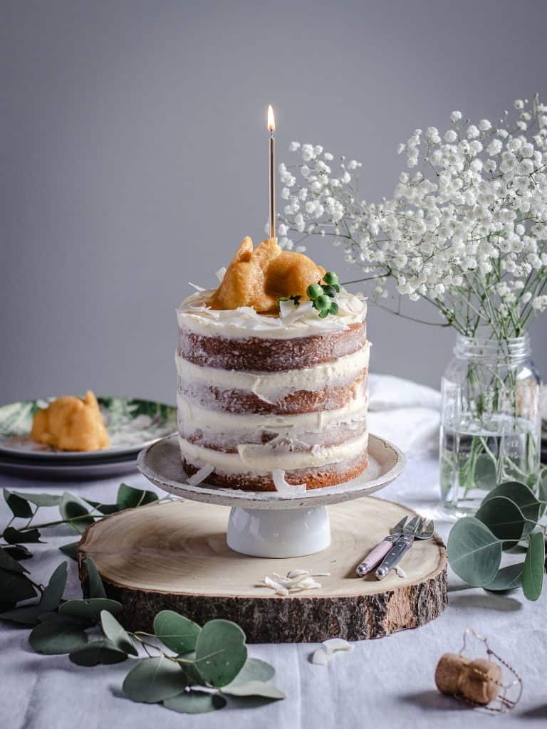 Tablescape with four layer lemon and coconut naked cake in center. Cake has a small bunny shaped cake on top with a lit gold candle