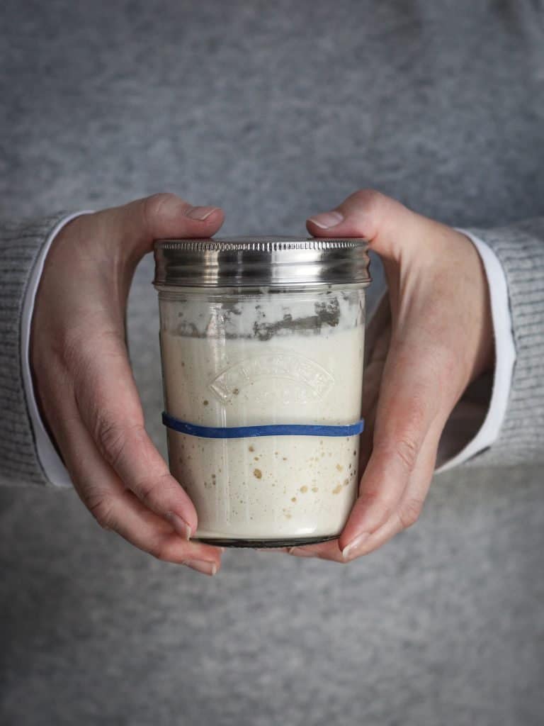 Two hands holding a glass jar with sourdough starter in it