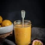 lemon and passionfruit curd in a glass jar with a tasting spoon in it