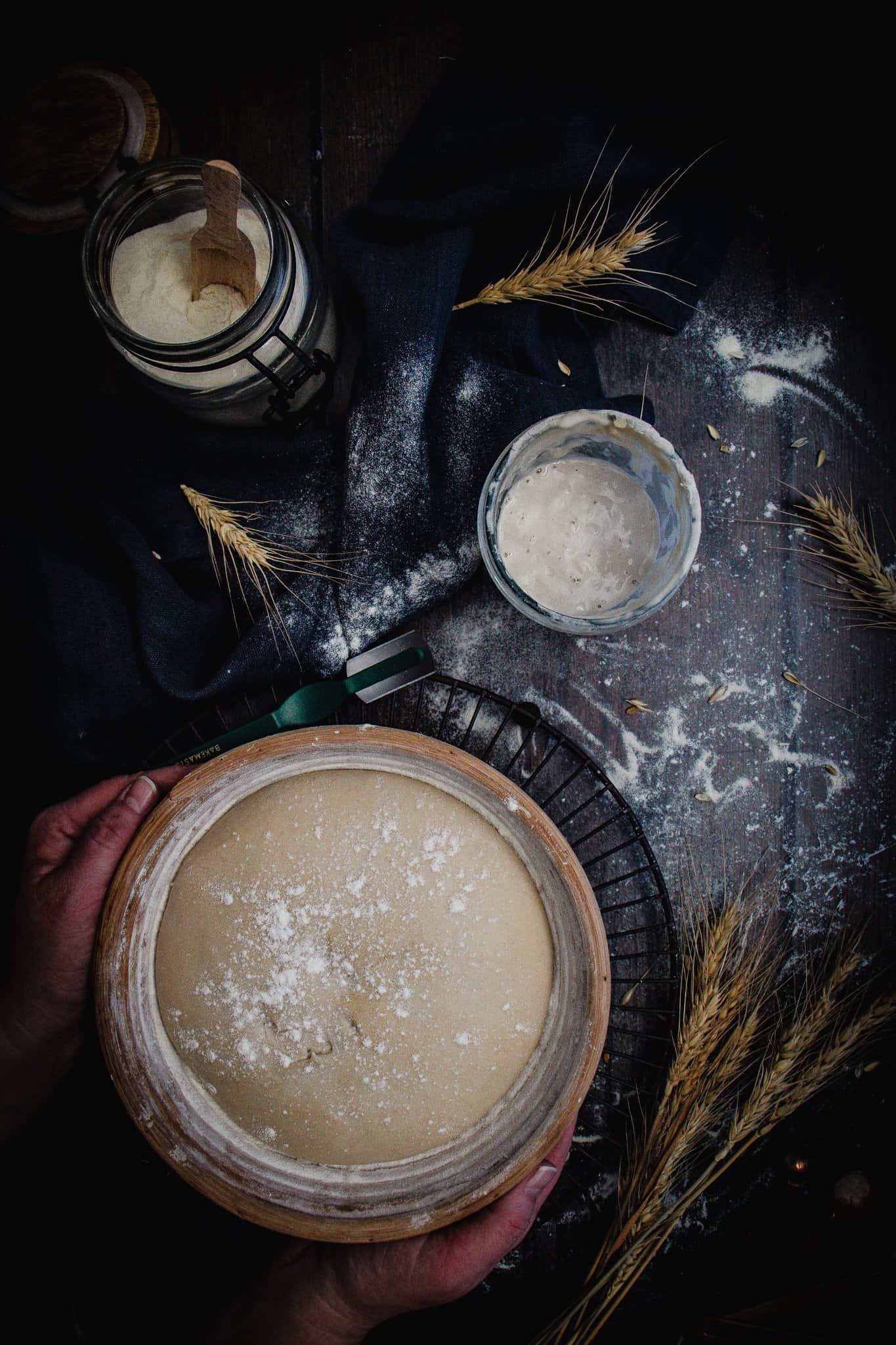 sourdough making. Dough in banneton being prepared for baking. Sourdough starter and lame beside.