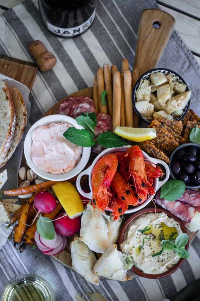 Round board full of meze. olives, dips, chargrilled vegetables, prawns, cured meats, breadsticks, crackers and sourdough.