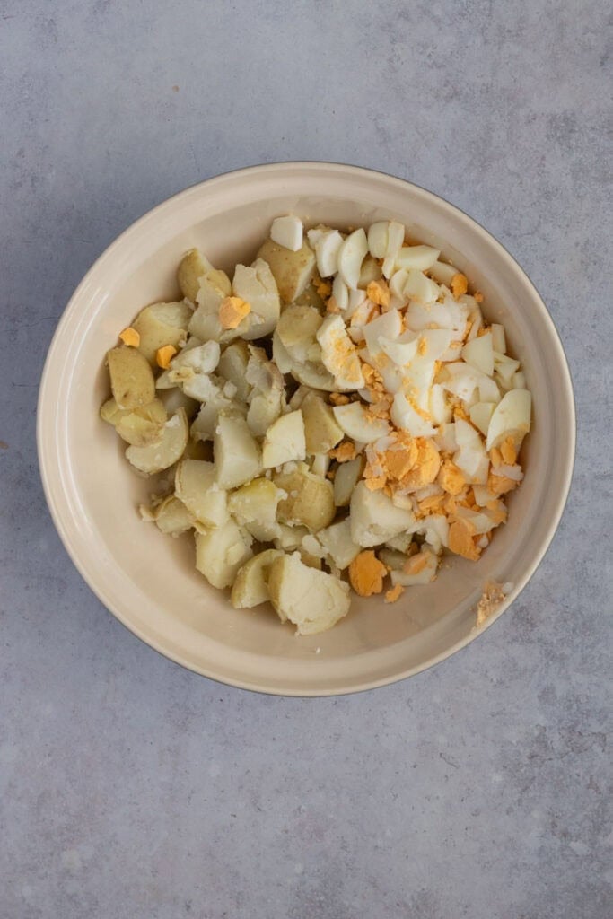 Chopped boiled potatoes and egg in a large ceramic bowl.