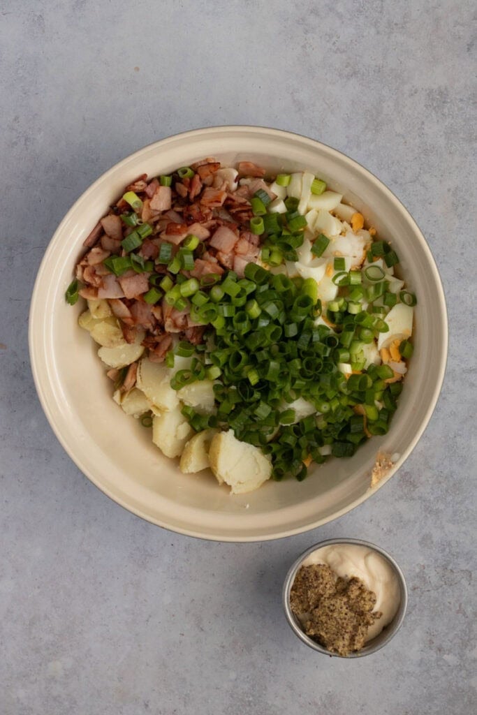 The cooked salad ingredient are in the bowl ready to be combined with the mayonnaise and mustard beside.