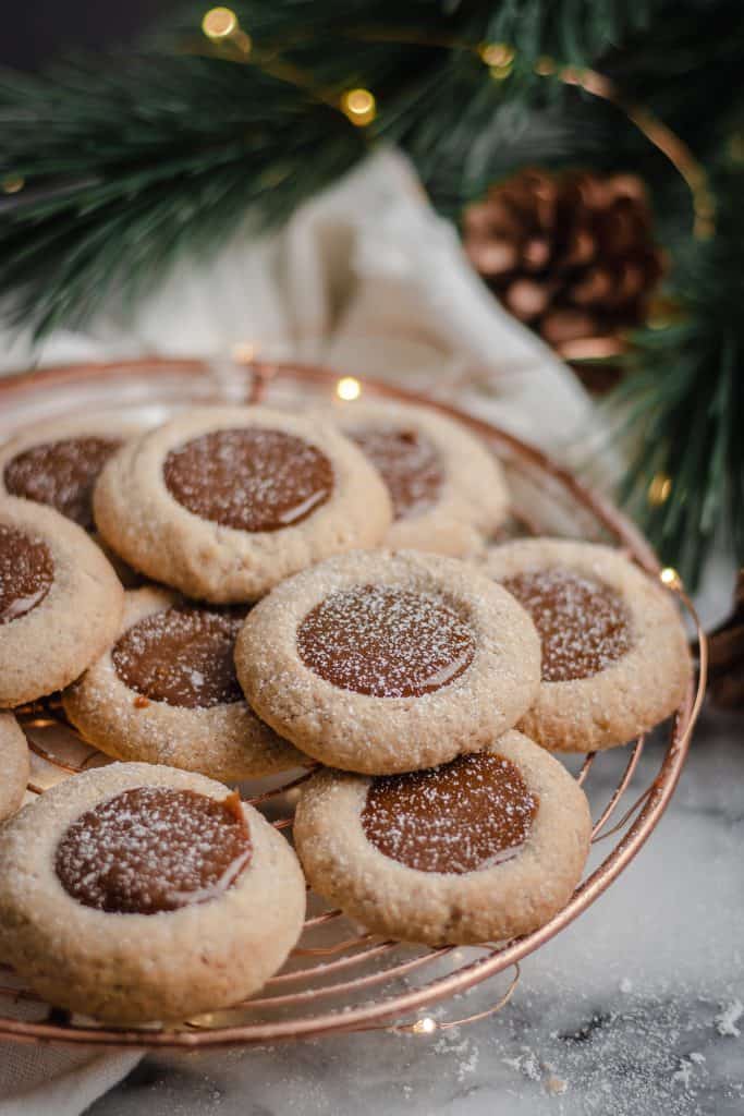 Spiced dulce de leche thumbprints on a copper cooling rack dusted in icing sugar