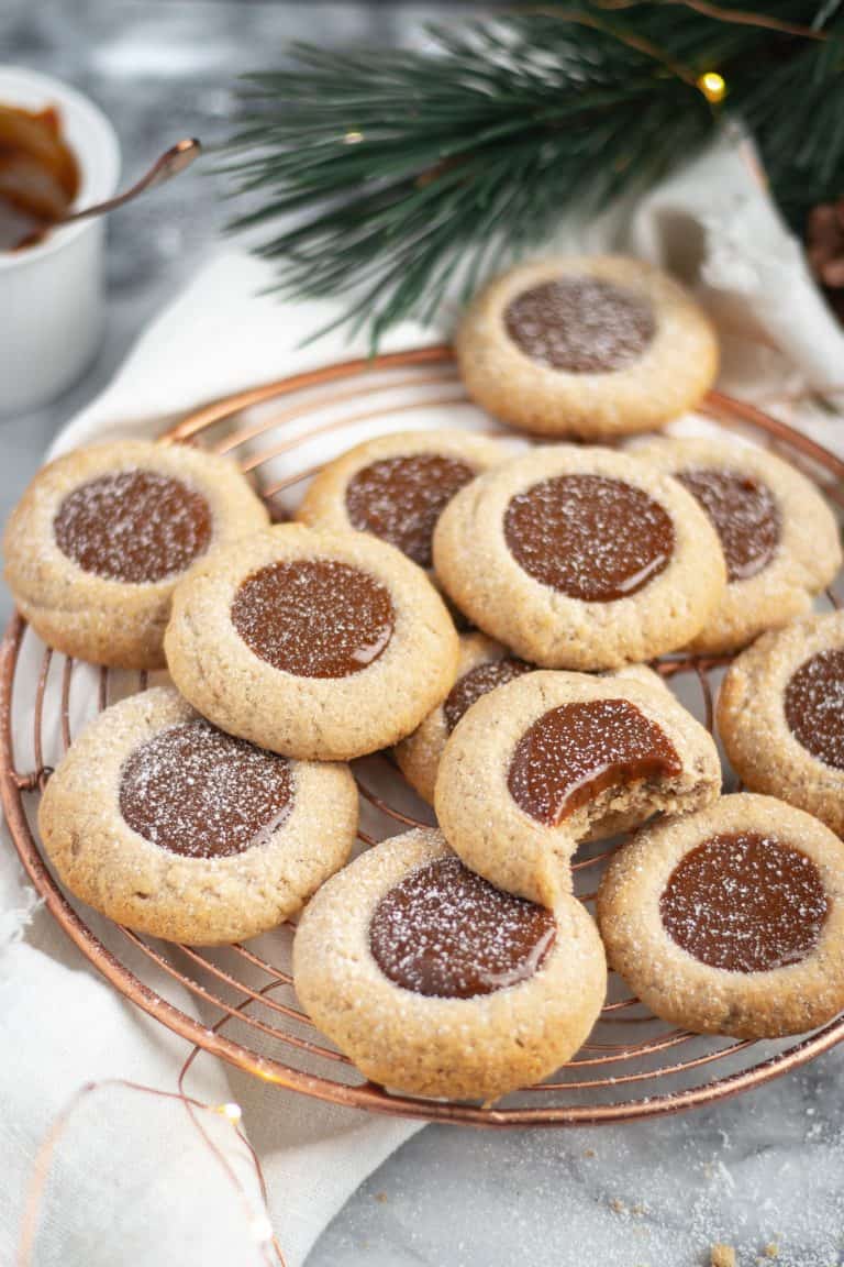 spiced dulce de leche thumbprints dusted with icing sugar on a copper cooling rack