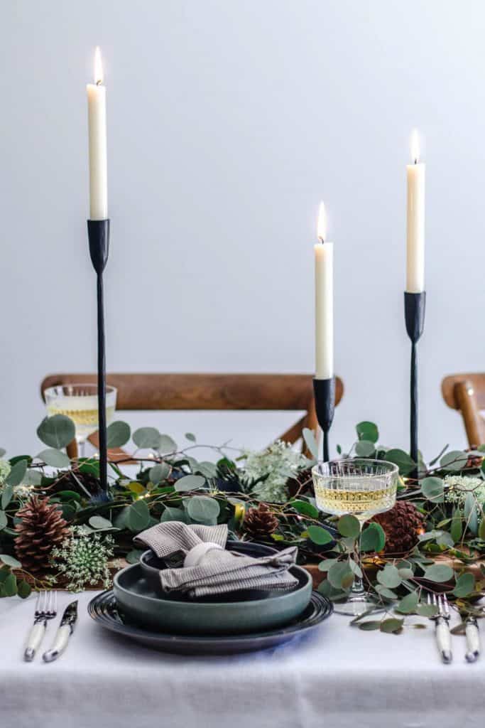 An easy Christmas table setting laid with greenery, servingware, glasses and champagne