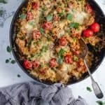 A cast iron frypan of chicken chorizo orzo bake with a spoon already dished out