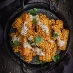 A stack of smokey chipotle corn ribs drizzled with lime mayonnaise and scattered coriander leaves
