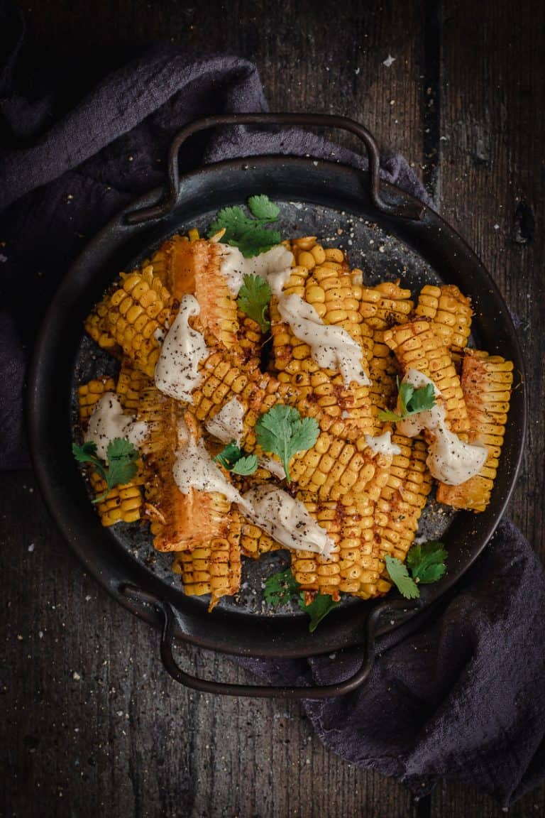 A stack of smokey chipotle corn ribs drizzled with lime mayonnaise and scattered coriander leaves