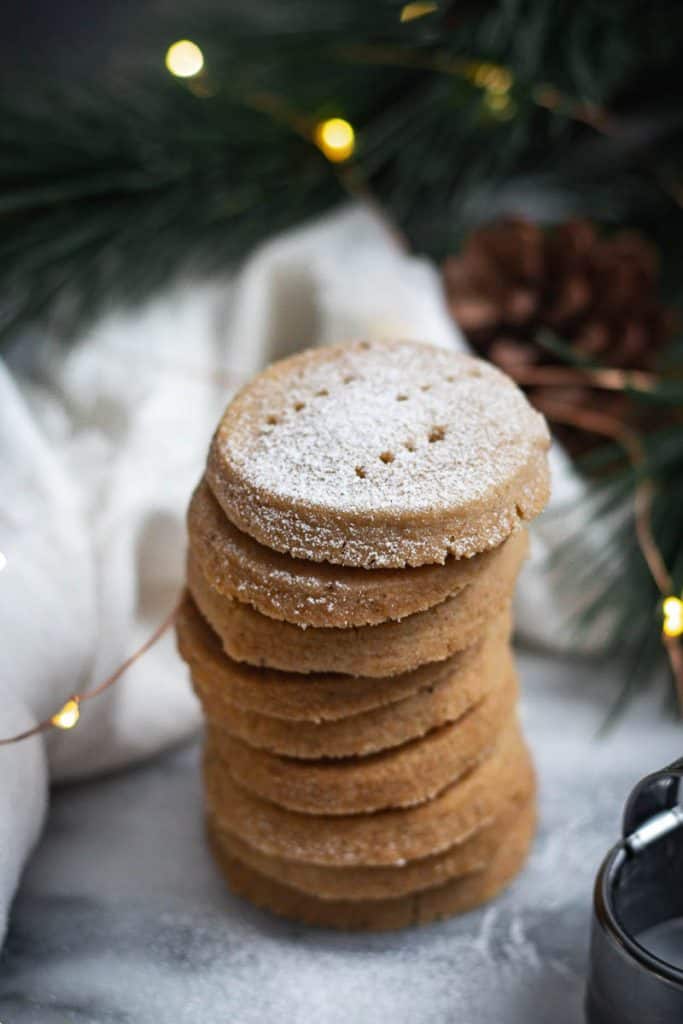 A stack of vanilla spiced shortbread cookies surrounded by Christmas tree branches and fairy lights