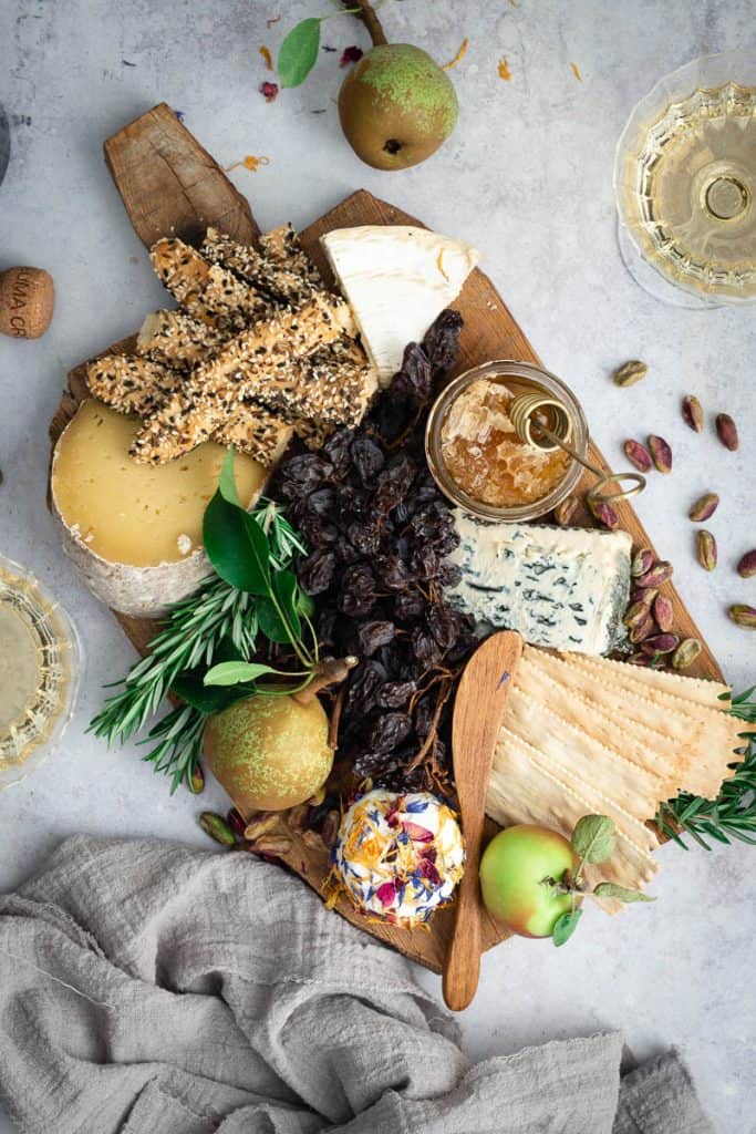 a cheeseboard for two full of cheese, crackers, fruit and nuts. Two glass of champagne sit near