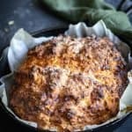 a load of bacon, chive and cheese soda bread in a black cast iron frypan on a floured surface