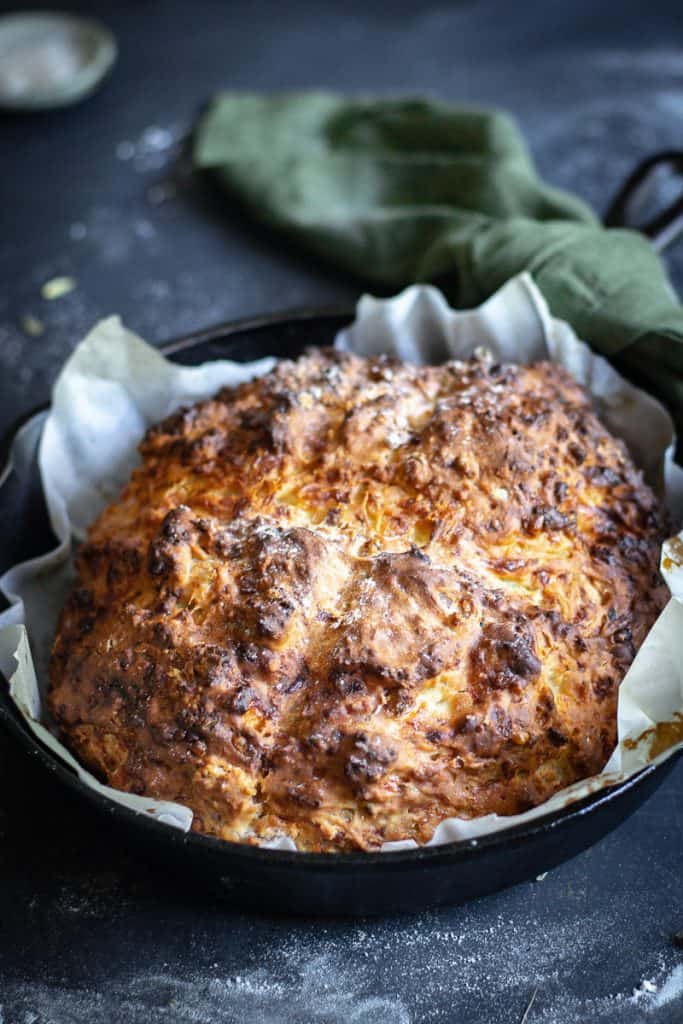 a loaf of bacon, chive and cheese bread in a cast iron frypan just out of the oven  on a floured table.