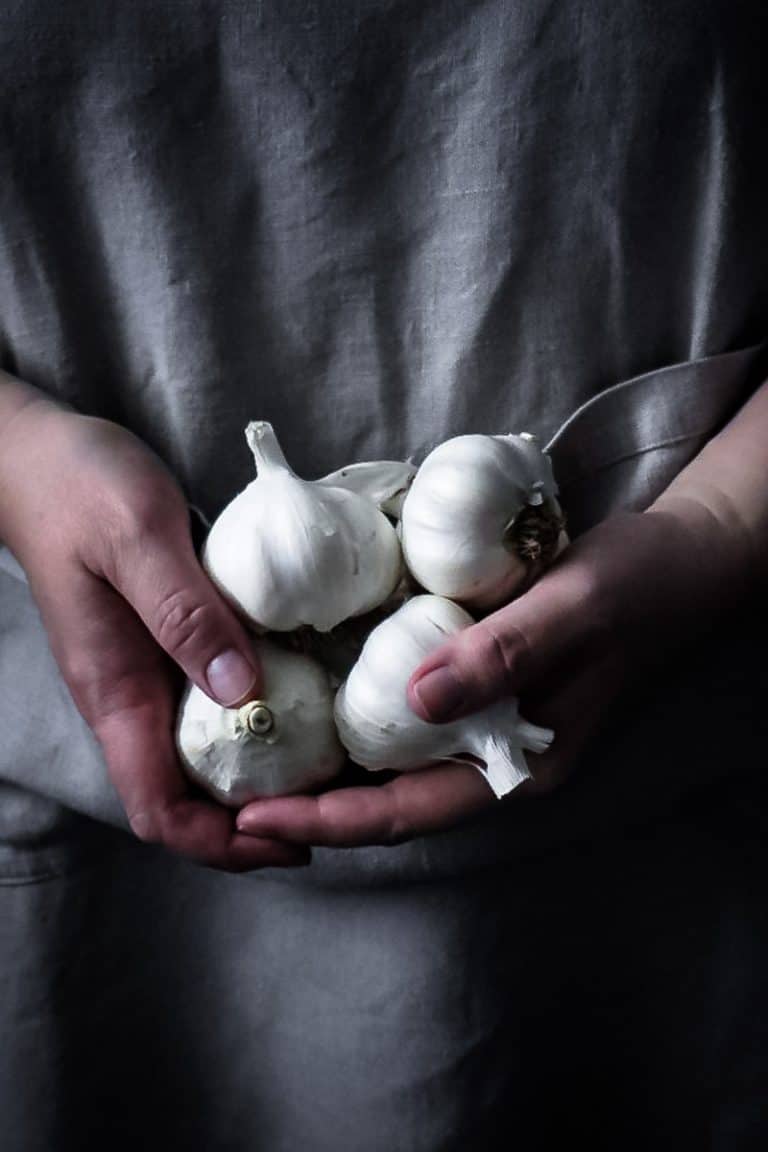 two hands holding a few bulbs of garlic