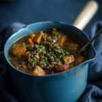 A enamel saucepan full of Persian lentil sweet potato soup with a spoon in it.