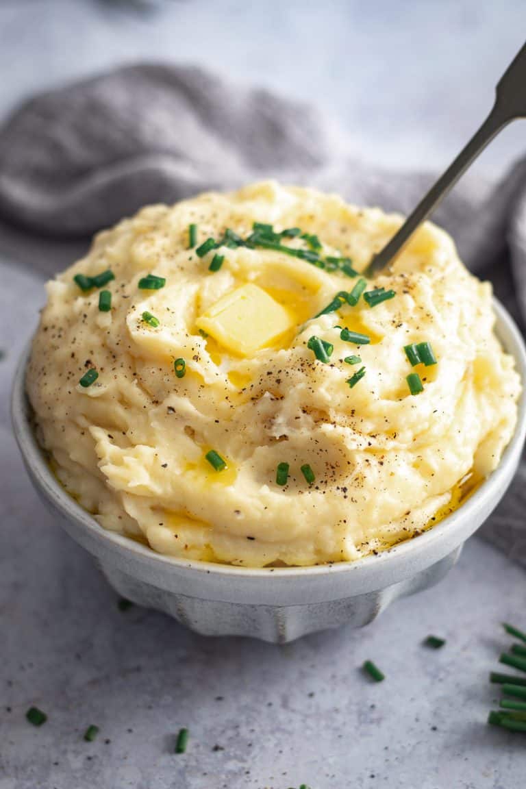 a bowl piled high of creamy mashed potato with a dob of butter on top and finished with a sprinkle of chives