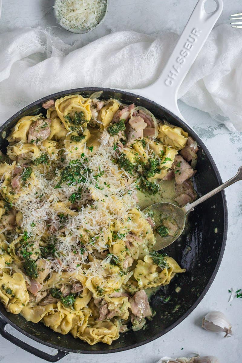 cast iron frypan full of creamy pesto chicken tortellini with a spoonful eaten out of it.