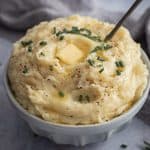 A bowl piled high of creamy mashed potato with a dob of butter on top and finished with a sprinkle of chives.