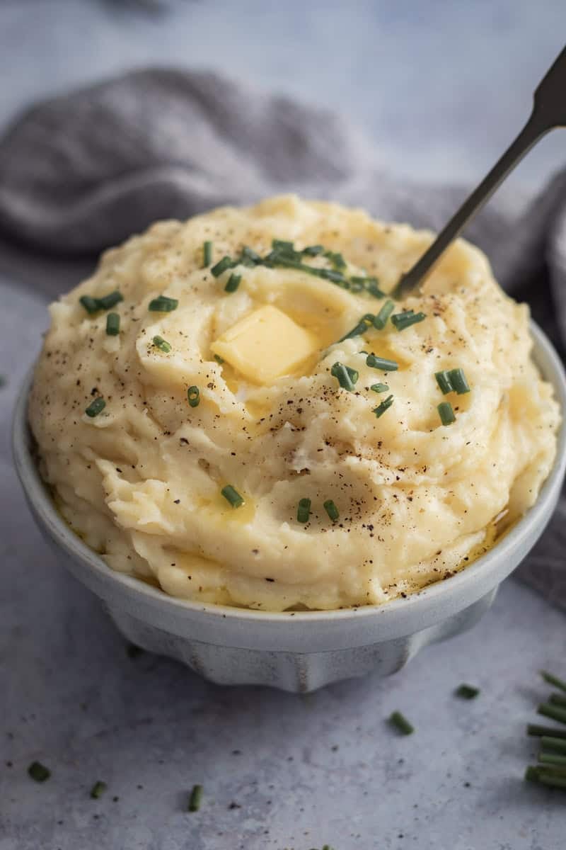 A bowl piled high of creamy mashed potato with a dob of butter on top and finished with a sprinkle of chives.