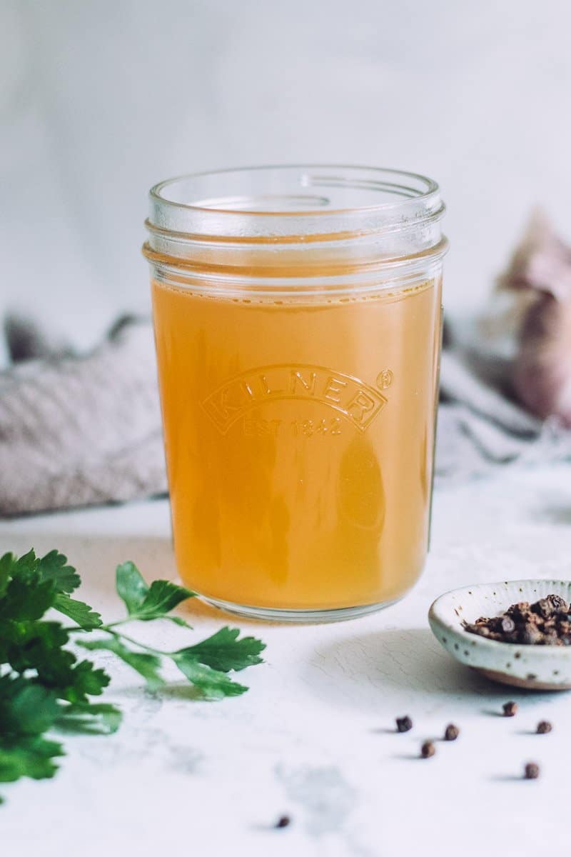 a jar of homemade chicken stock made in a pressure cooker. There is a bunch of parsley, some garlic and peppercorns on the bench around the jar