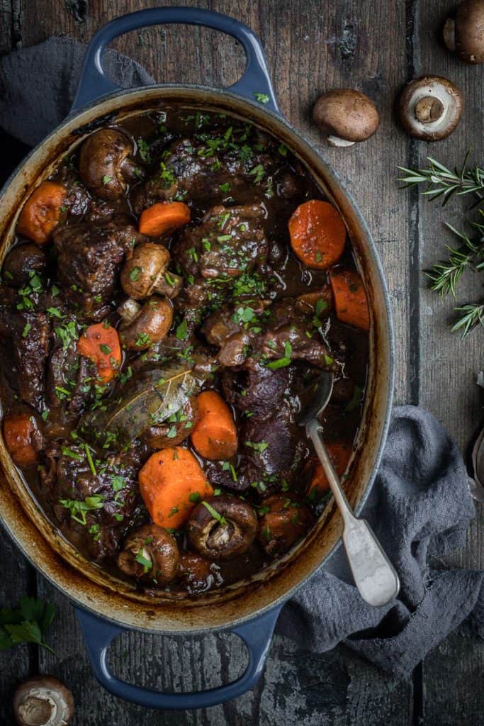 a oval cast iron french oven full of slow cooked beef cheeks in red wine with carrots and mushrooms.