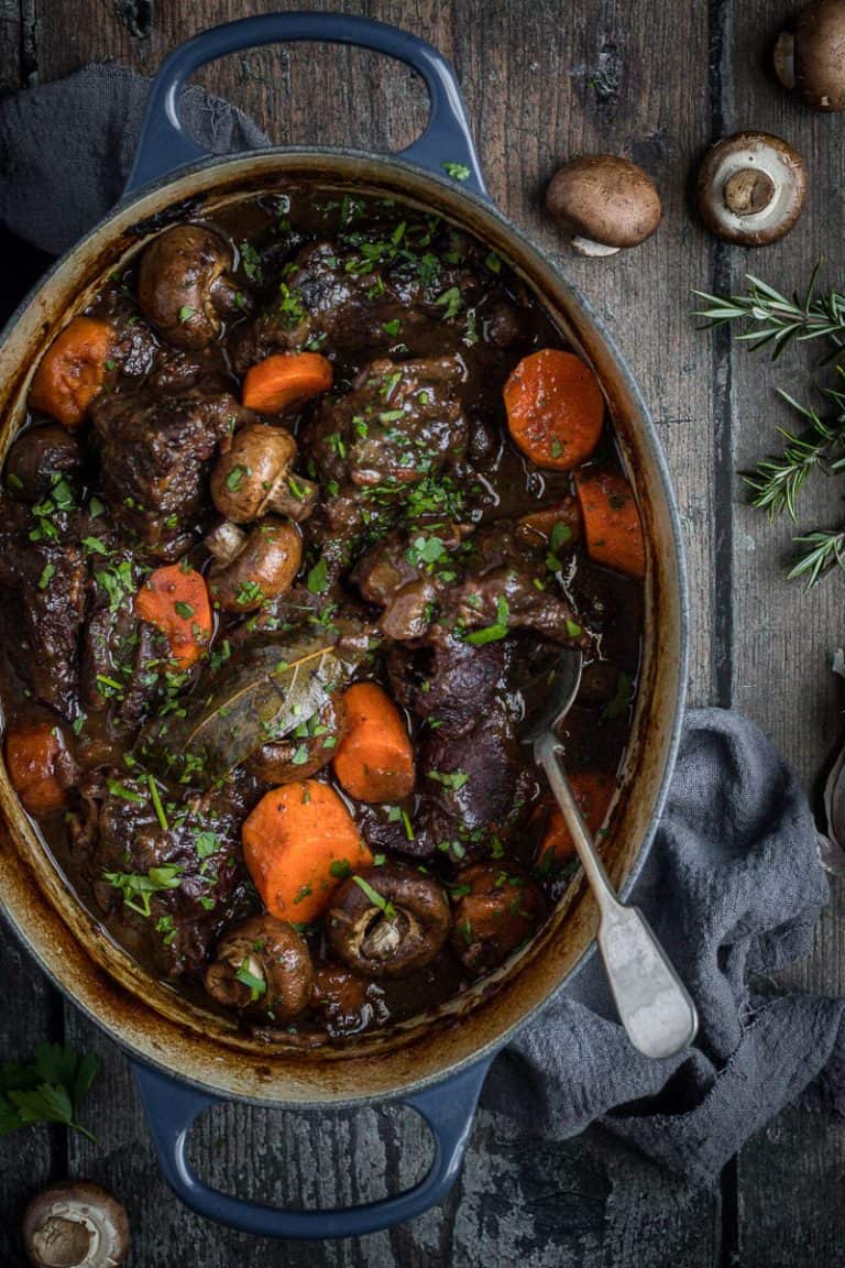 a oval cast iron french oven full of slow cooked beef cheeks in red wine with carrots and mushrooms.