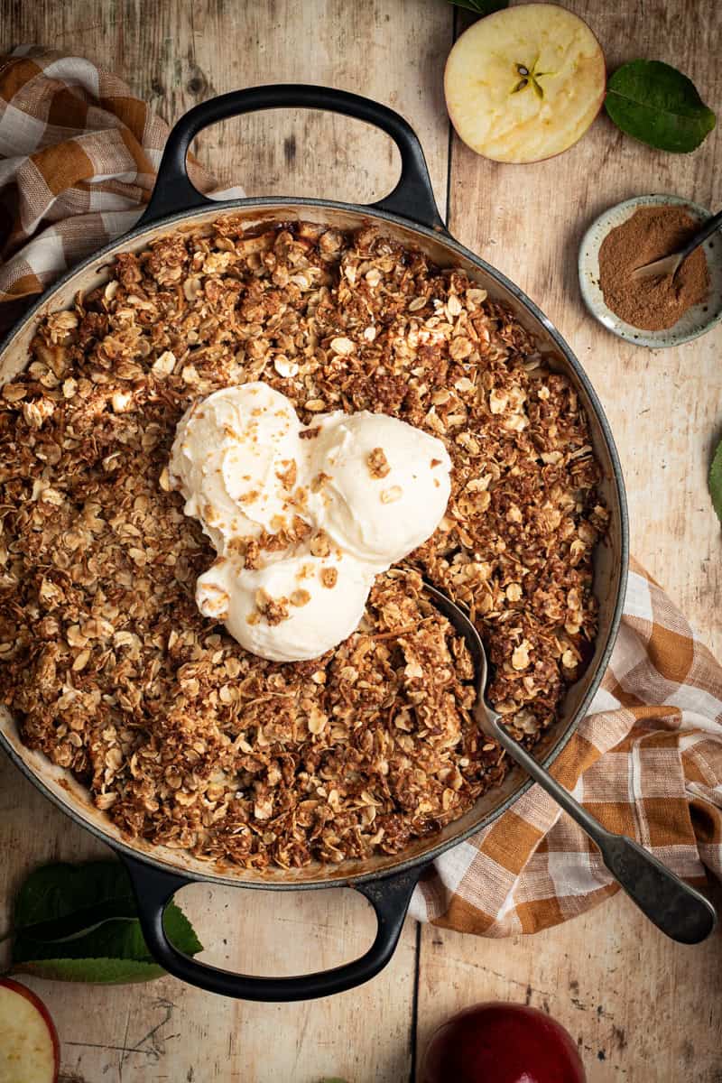 A close up of a skillet apple crumble with scoops of ice cream on top.