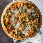 a white pan of chicken and chorizo risotto with a check linen towel tied around the handle