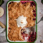 a blackberry and apple crumble on a bench with a scoop eaten and ice cream on top