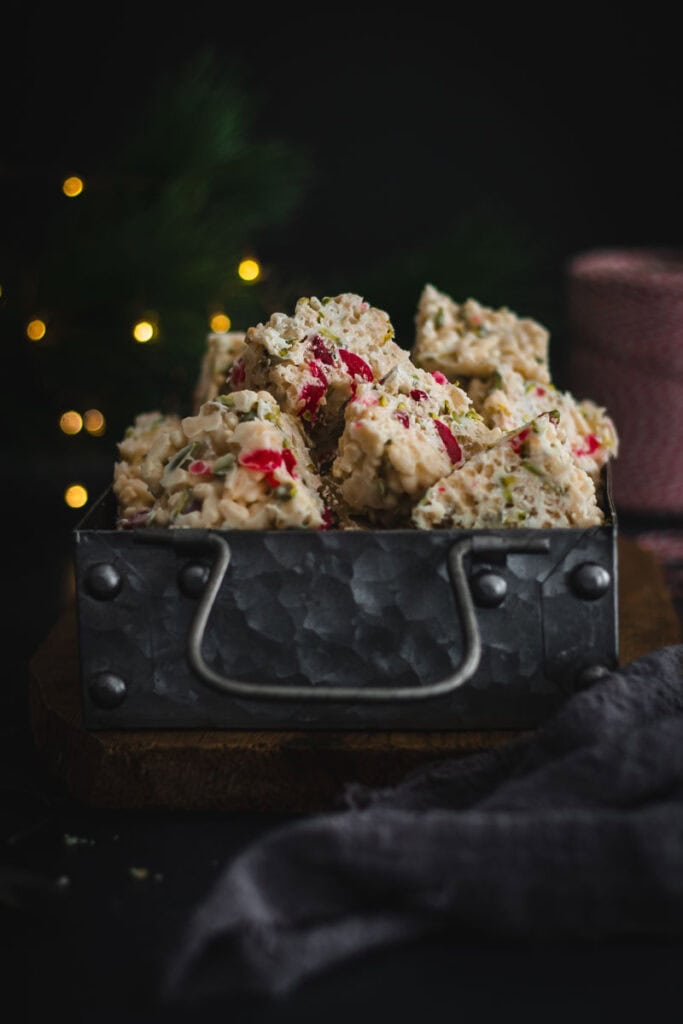 A tin of white Christmas slice with twinkling fairy lights behind.