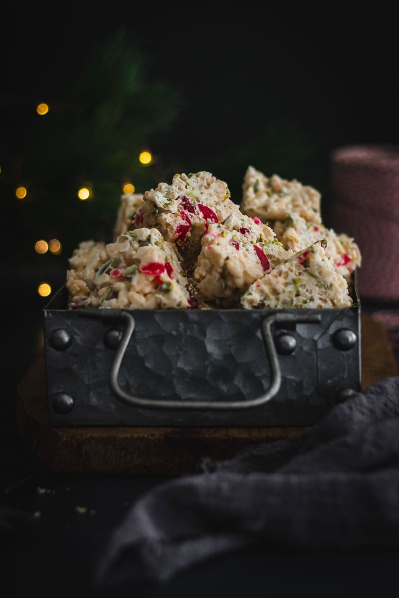 A tin of white Christmas slice with twinkling fairy lights behind.