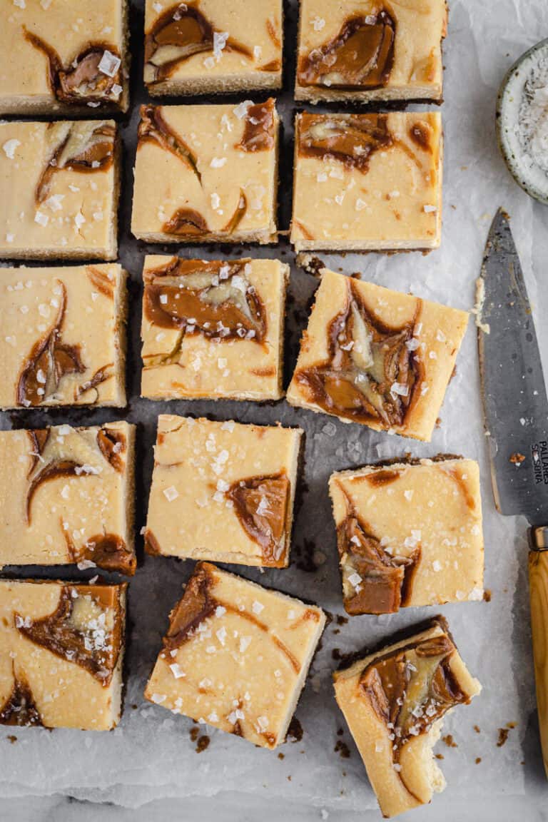 flatlay of a tray of baked biscoff cheesecake slice cut into squares with a bite taken out of one piece