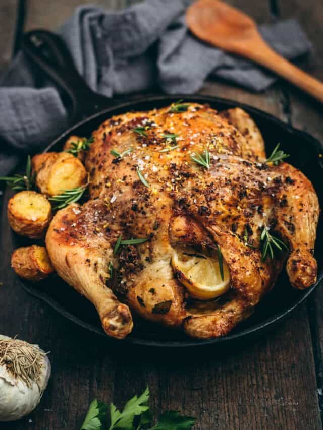 A Greek roast chicken in a black cast iron skillet with potatoes and fresh herbs