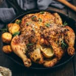 A Greek roast chicken in a black cast iron skillet with potatoes and fresh herbs.