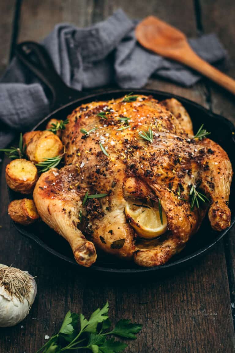A Greek roast chicken in a black cast iron skillet with potatoes and fresh herbs.