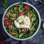 a bowl of pesto orzo salad with a whole burrata drizzles with pesto and extra virgin olive oil on top