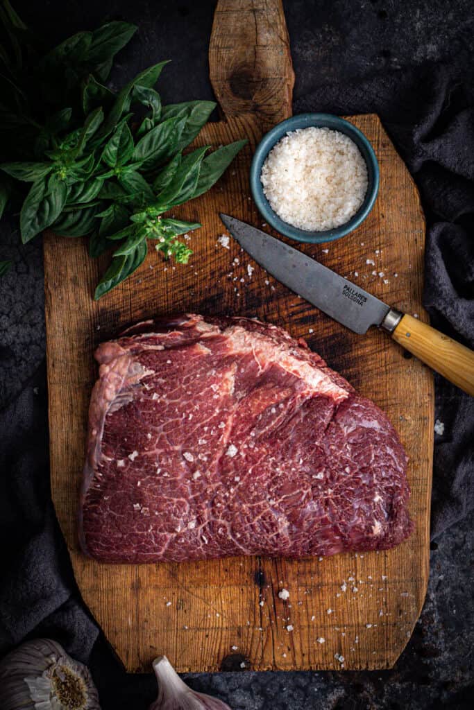 a beef cheek sprinkled with sea salt flakes sits on a chopping board ready for cooking