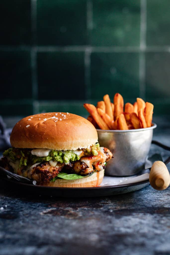 a grilled cajun chicken burger with a side of fries on a metal plate