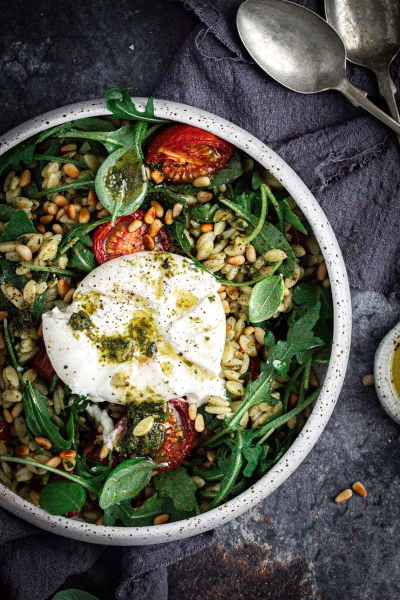 A bowl of pesto orzo pasta salad with a whole burrata drizzles with pesto and extra virgin olive oil on top.