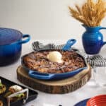 A baked apple french toast in a blue cast iron frypan on a set table of other blue and orange cookware pieces.