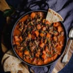 A black pot of Persian lamb shank and vegetable soup with naan bread.