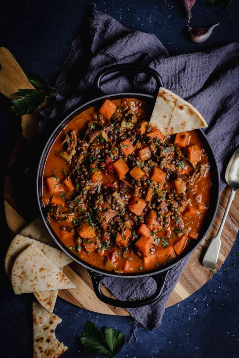 A black pot of Persian lamb shank and vegetable soup with naan bread.