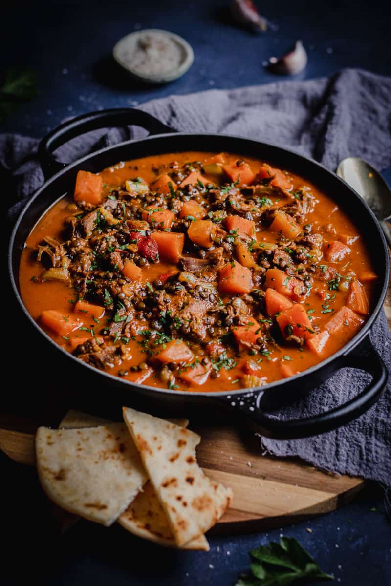 A black pot of Persian lamb shank and vegetable soup with naan bread on the side.