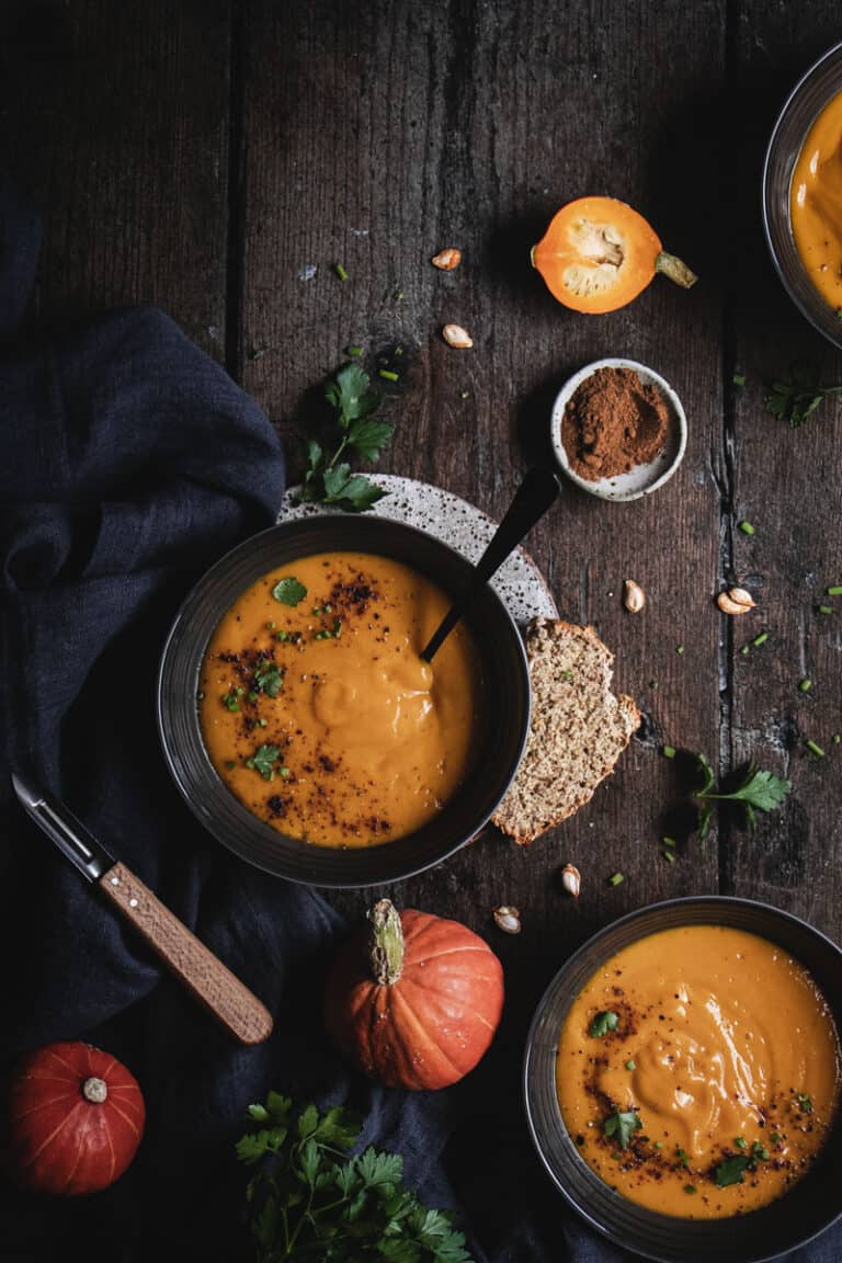 two bowls of roast butternut chipotle soup without cream on a timber bench.