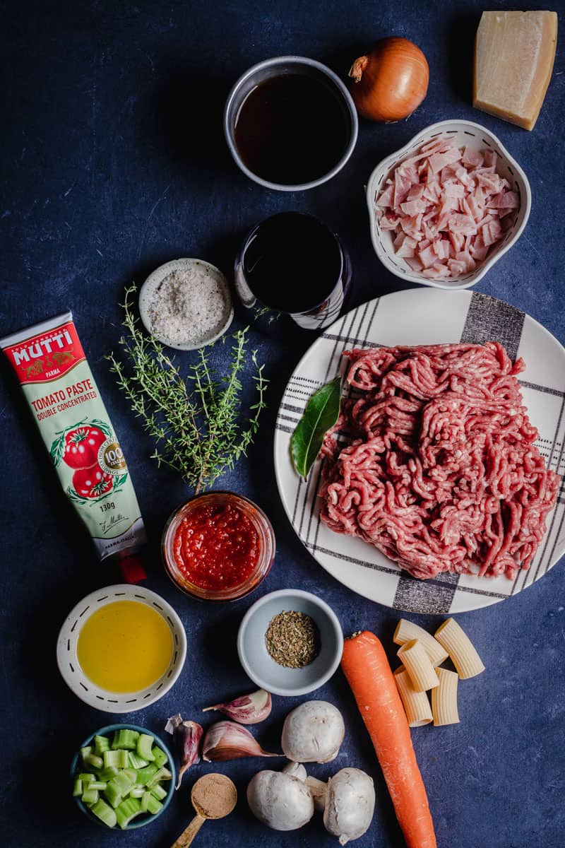 An ingredient shot of everything you need to cook slow-cooked Rigatoni Bolognese in a Dutch oven
