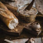A jar of homemade black garlic butter on a board alongside a chunk of crusty baguette.