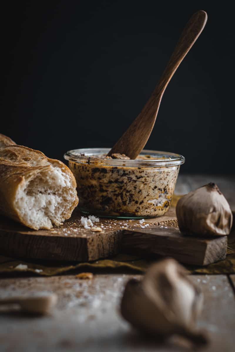 a jar of homemade black garlic butter with a wooden knife stuck in the jar.