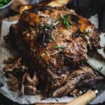 A Slow-cooked lamb shoulder with some of the meat pulled apart on a timber chopping board.