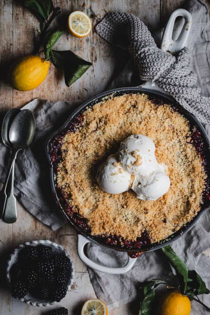 The baked apple and blackberry crumble in a cast iron skillet topped with scoops of vanilla ice cream.